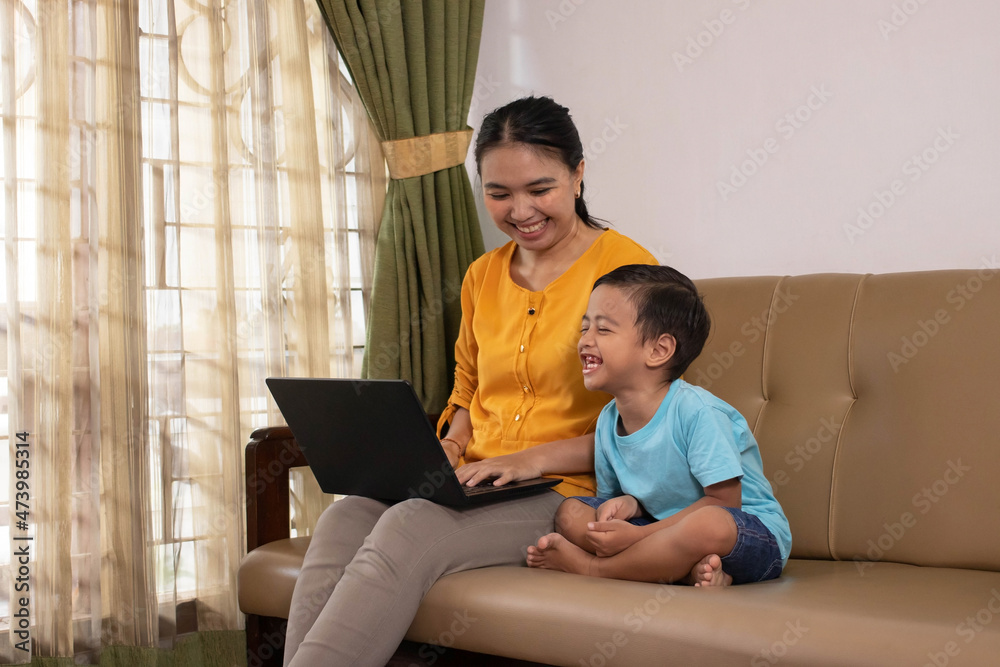 Fototapeta premium Beautiful Asian business mom uses a laptop and spends time with her son