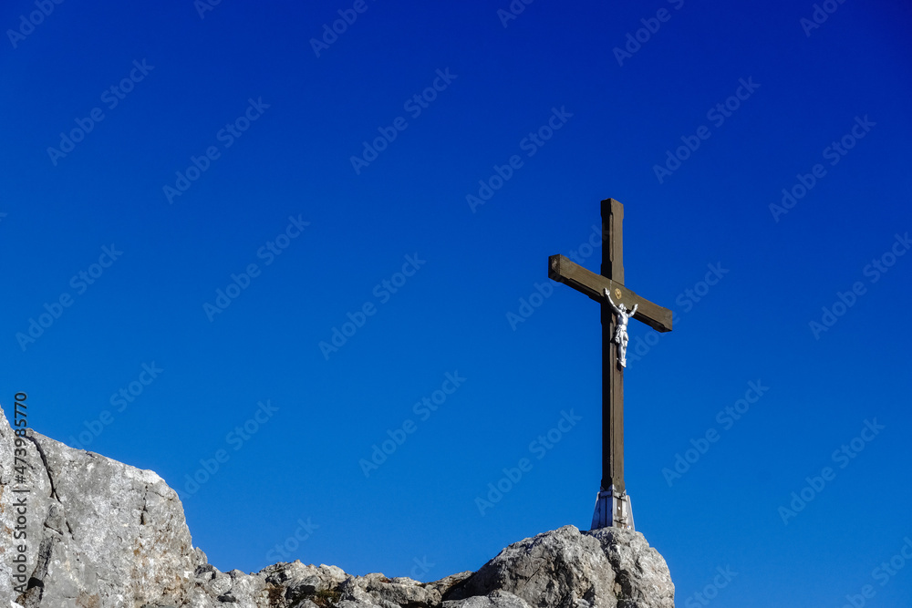 wooden cross with white jesus statue on the rocks at the summit with dark blue sky