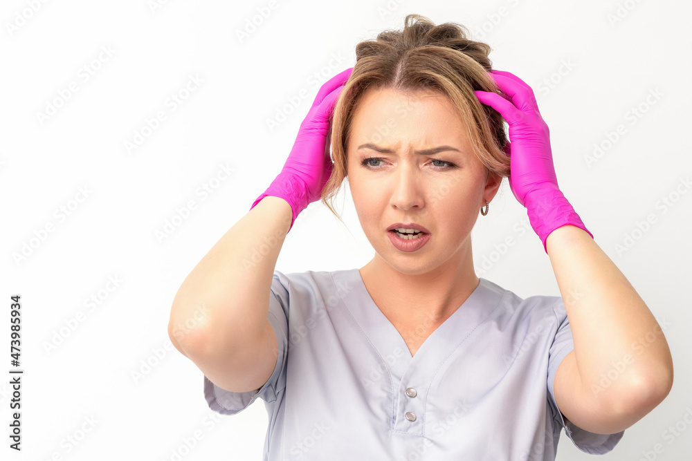 The emotionally shocked young female medical worker holding hands on her head fell into panic on white background, infection, epidemic, virus, and disease concept