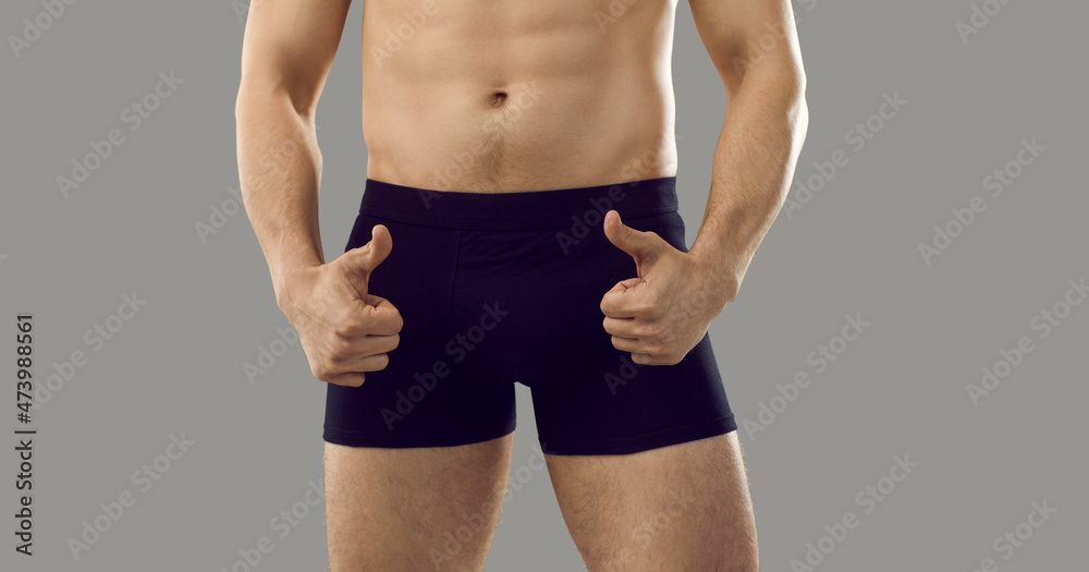 Fototapeta premium Young macho man who takes viagra is showing thumbs up standing isolated on grey background. Handsome male in boxer briefs with good sexual health and fit attractive body advertises impotence treatment