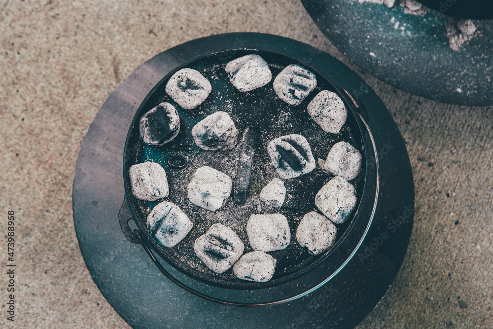 dutch oven covered with light gray coals for cooking in it