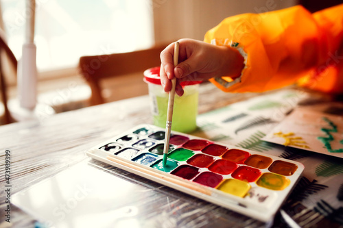 cute caucasian child Toddler is engaged in creativity in a yellow protective apron, the child draws with paints on salt, unusual drawing and developmental activities