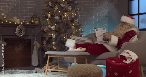 Santa Claus reading magazine and eating tasty gingerbread cookies at home