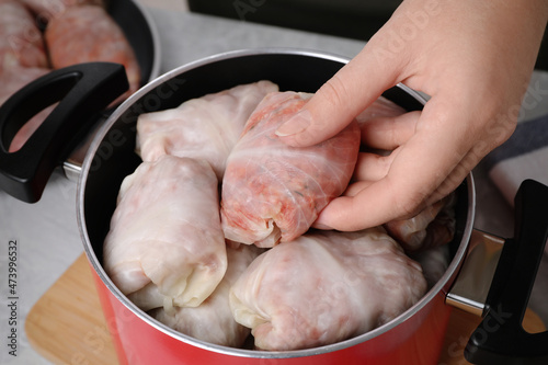 Woman putting uncooked stuffed cabbage roll into pot at light grey table, closeup