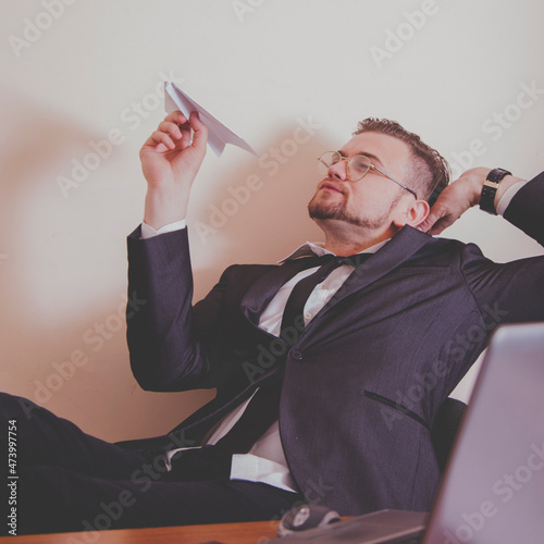 Conceptual image: professional burnout, laziness, unwillingness to work. Close up portrait of slacker businessman sitting in office with legs on the table and playing with paper plane. photo