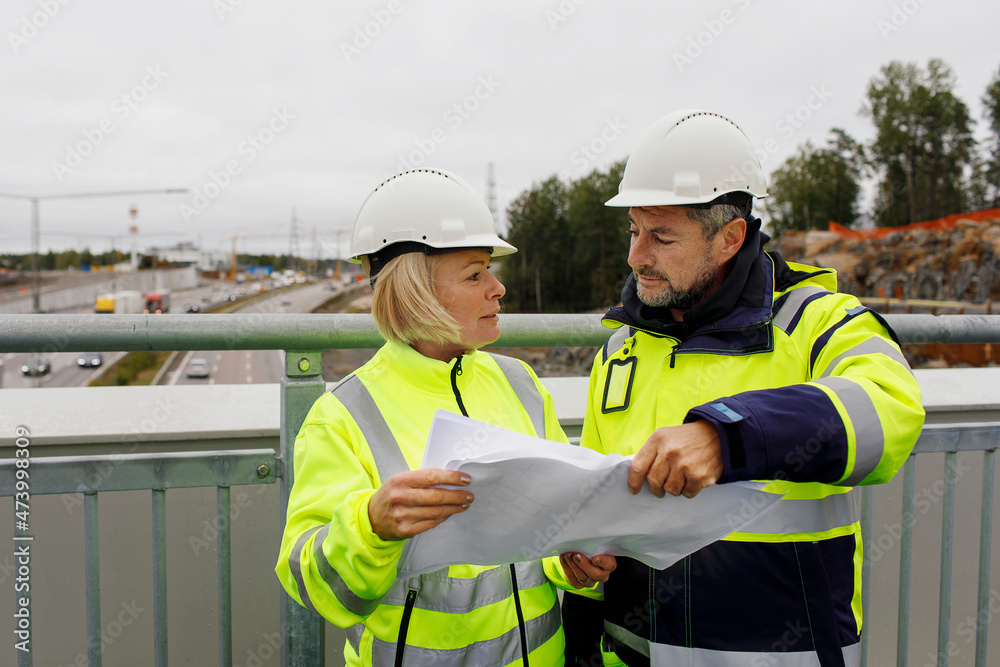 Engineers in reflecting clothing looking at blueprints Engineers in reflecting clothing looking at blueprints