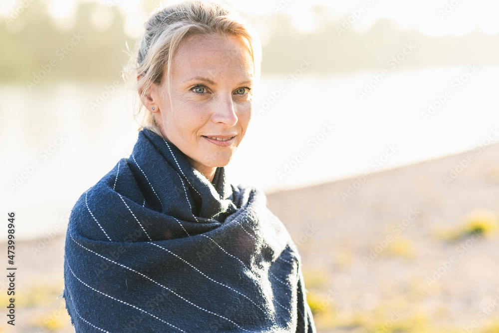 Smiling woman wrapped in blanket at riverbank