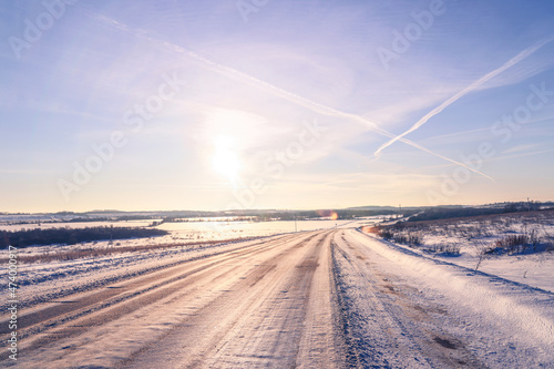 Winter landscape. Road, snow fields, blue sky with clouds and bright sun. Beautiful nature background 