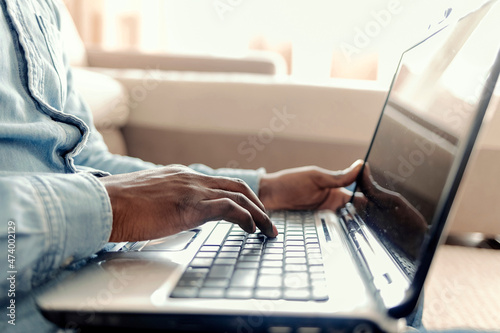 Handsome young man smiling while using a laptop while sitting on the floor in his living room at home. Portrait of a young man using laptop at home.