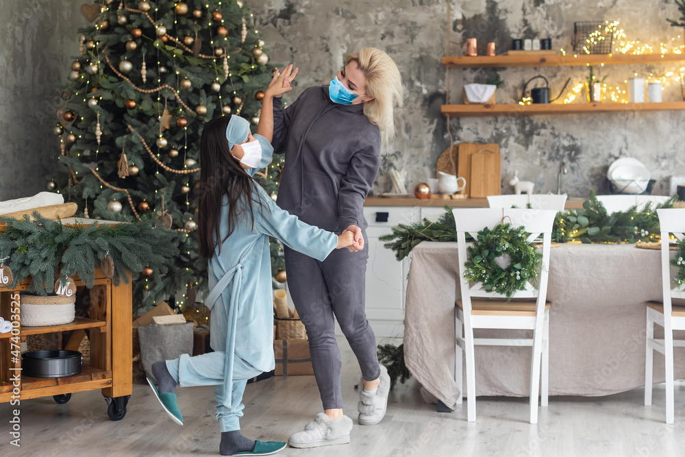Obraz premium mother and daughter wearing medical masks under the christmas tree during home celebration