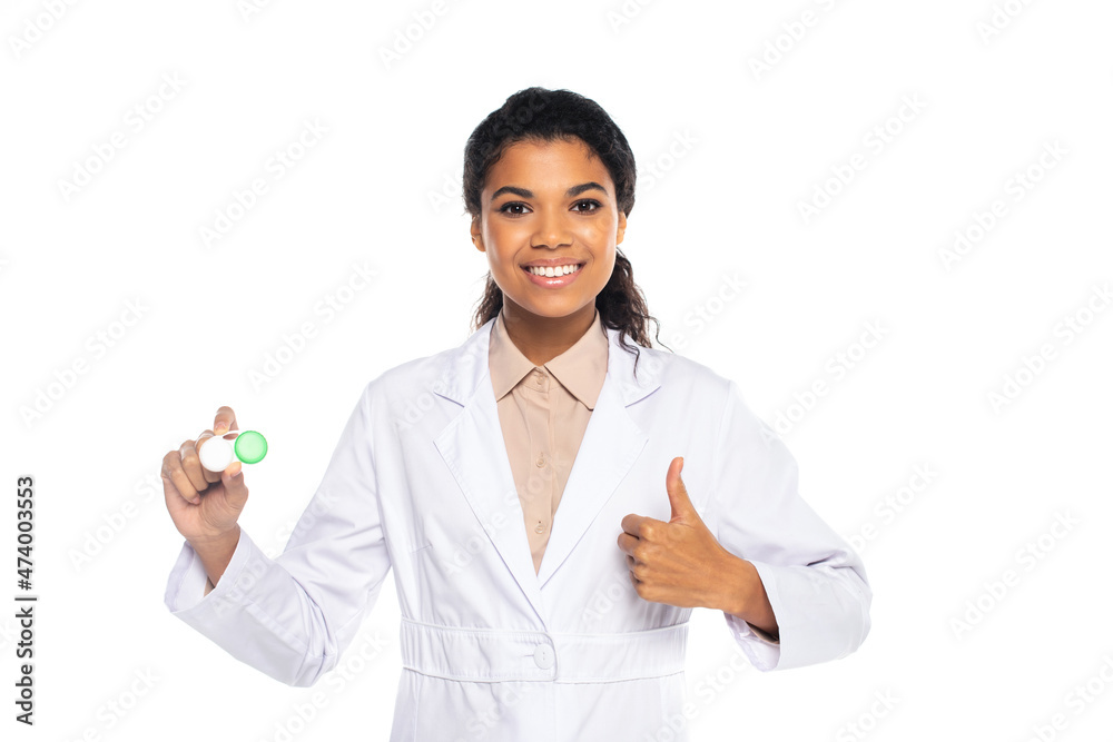 Smiling african american doctor in white coat holding container with lenses and showing thumb up isolated on white. Smiling african american doctor in white coat holding container with lenses and showing thumb up isolated on white.
