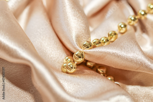 Shiny golden textured silk background in folds with beads.