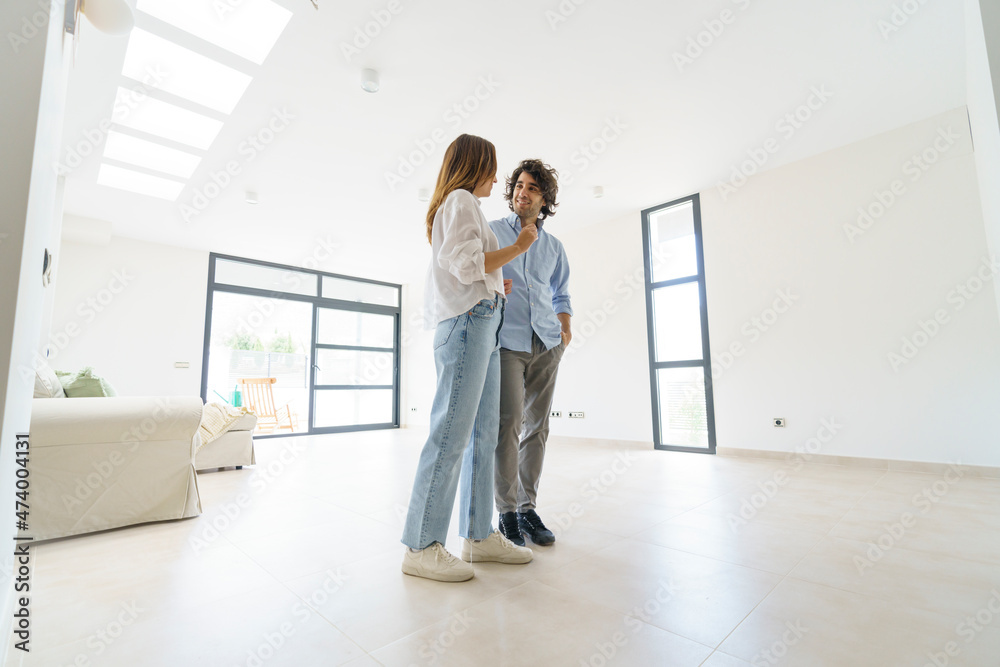 Smiling couple talking while standing in living room at home Smiling couple talking while standing in living room at home
