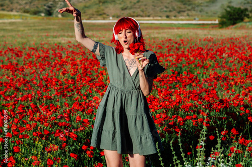 Young woman holding bunch of flowers while singing on poppy field photo