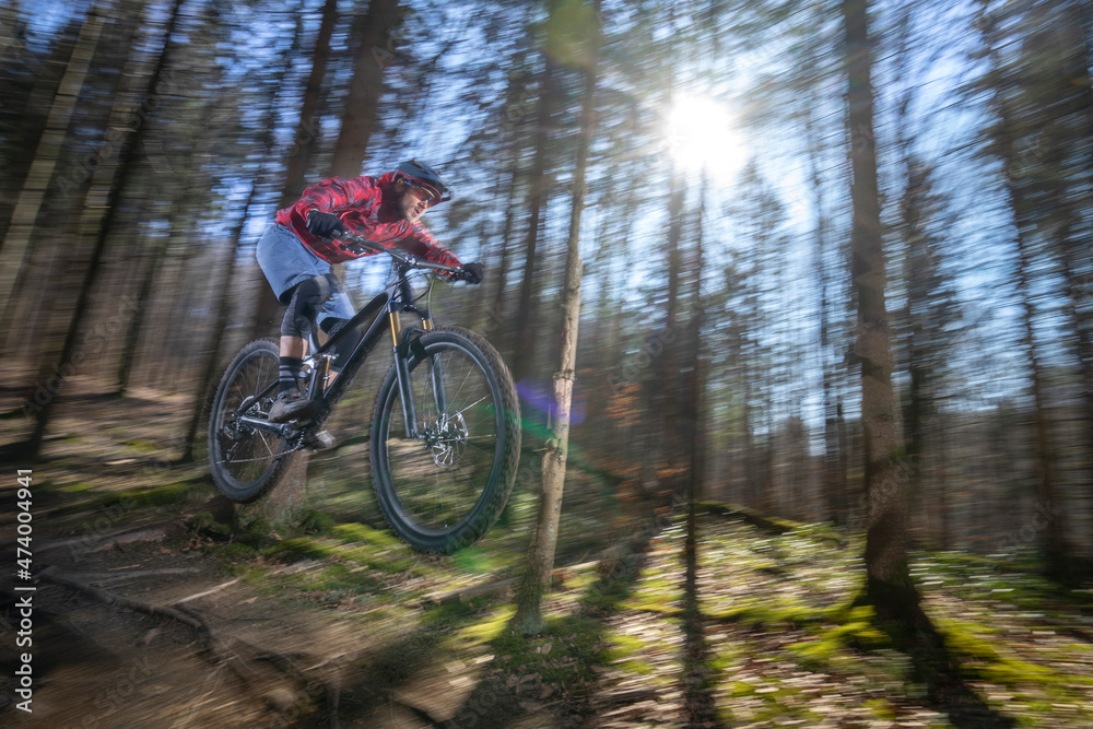 Male athlete in mid-air with mountain bike in forest Male athlete in mid-air with mountain bike in forest