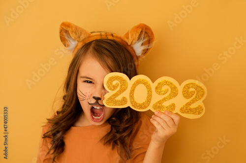 Girl with a painted face in the guise of a tiger growls with her mouth open, holding the number 2022 in hands. New Year of the tiger according to the Eastern calendar. Big discounts, pre-holiday sales