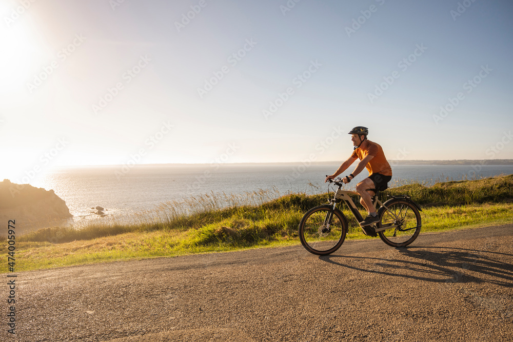 Mature sportsman cycling bicycle on road near sea at sunset