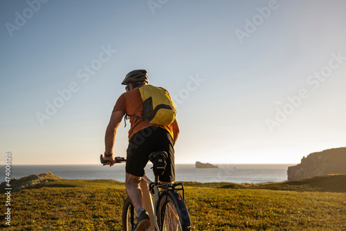 Male athlete with backpack riding mountain bike towards sea photo