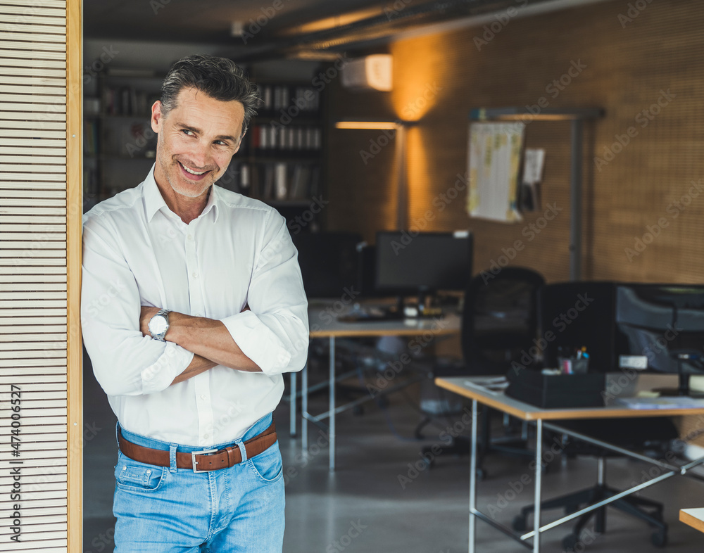 Confident businessman with arms crossed leaning on office door Confident businessman with arms crossed leaning on office door