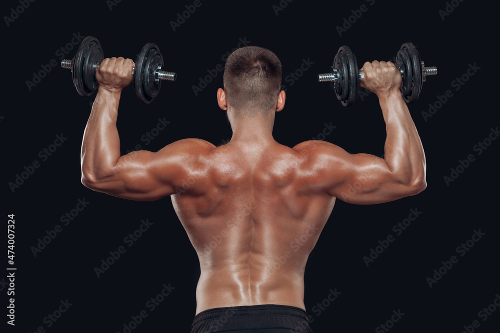 Close up back view of muscular body and strong hands lifting heavy dumbbells isolated over black background