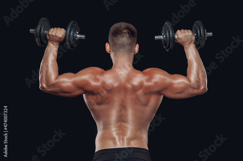 Close up back view of muscular body and strong hands lifting heavy dumbbells isolated over black background