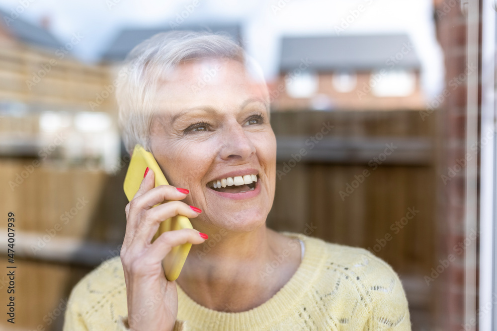 Happy mature woman talking on smart phone while looking through glass window Happy mature woman talking on smart phone while looking through glass window