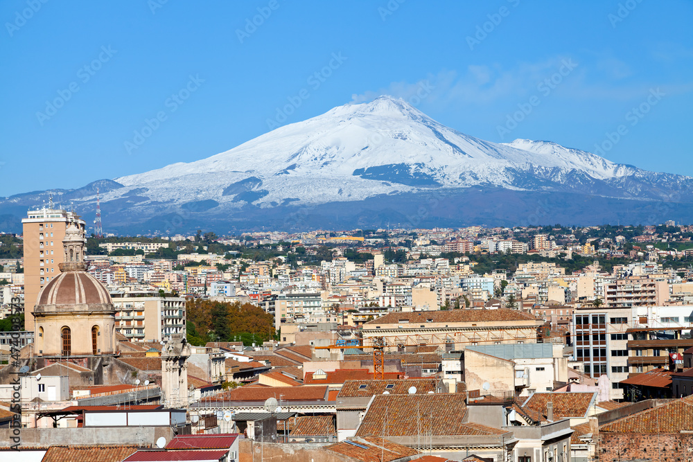 Panoramic view over Catania with the snowy volcano Etna behind city houses