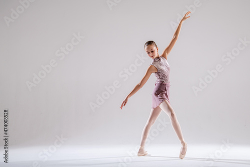 Beautiful young girl ballerina in pointe shoes and pink swimsuit on light background.
