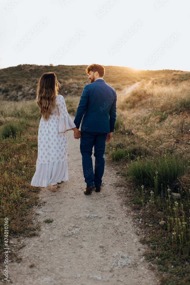 Couple holding hands while walking together during sunset Couple holding hands while walking together during sunset