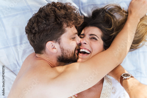 Shirtless man embracing cheerful girlfriend lying on picnic blanket photo