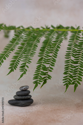 Photography Pyramids of gray zen pebble meditation stones with green leaves on beige background