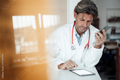 Male healthcare worker using digital tablet while leaning on desk in clinic photo