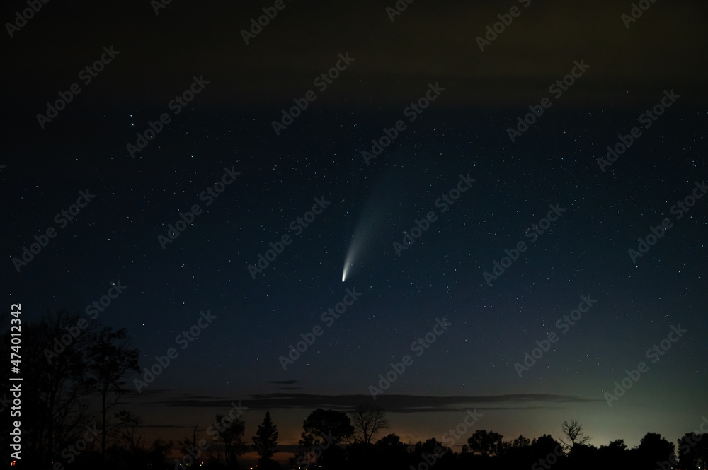 Bright comet Neowise above a calm night scene with a sailboat and pier reflecting in the still water.
