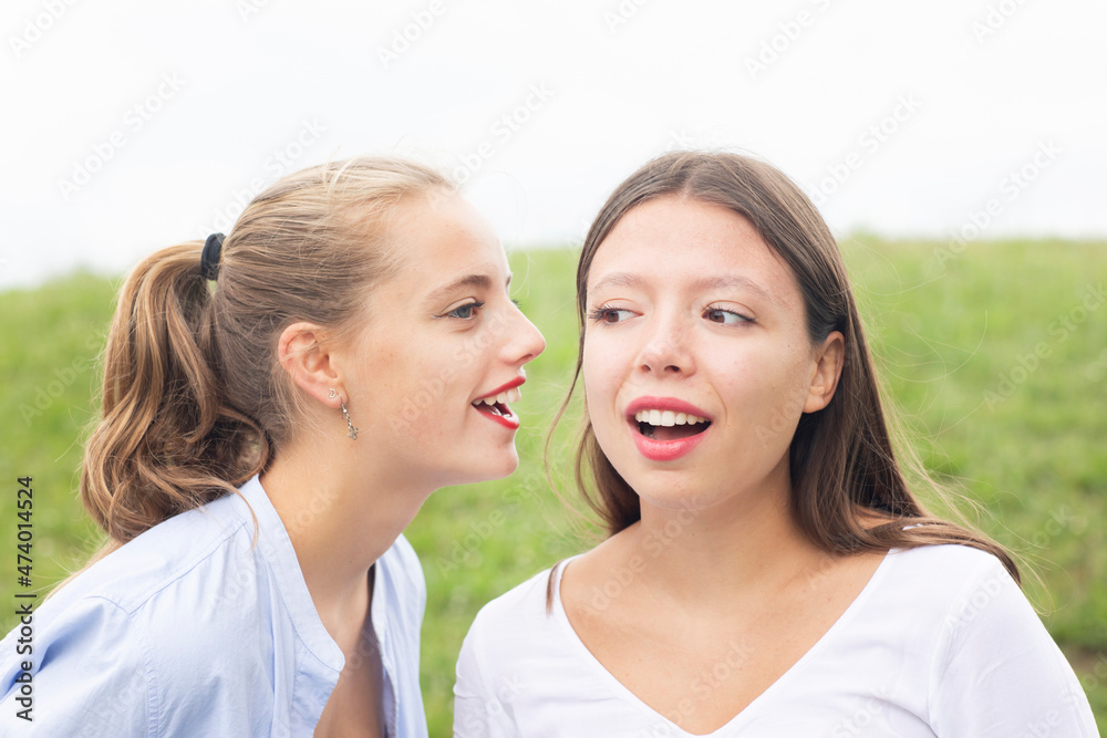 Young woman whispering to female friend in nature Young woman whispering to female friend in nature