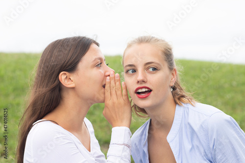Woman with brown hair gossiping in ear of female friend in nature photo