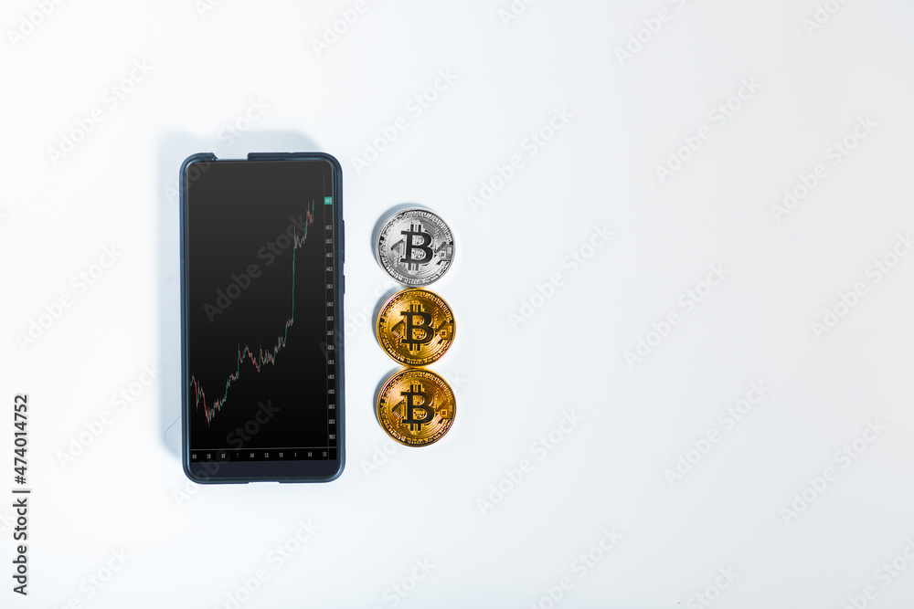 Phone with trand up of bitcoin. Bitcoin phisical money in wjite background Phone with trand up of bitcoin. Bitcoin phisical money in wjite background