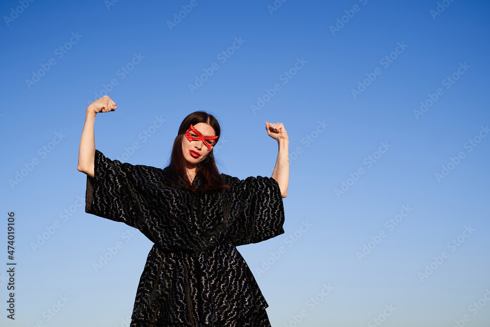 Female power, women rights, feminism activist concept. Portrait of strong woman in black dress and red face mask making fist pump, protesting for freedom and equality outdoor. High quality photo Female power, women rights, feminism activist concept. Portrait of strong woman in black dress and red face mask making fist pump, protesting for freedom and equality outdoor. High quality photo