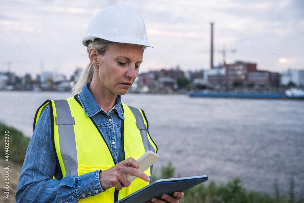 Female professional holding smart phone while using digital tablet during sunset Female professional holding smart phone while using digital tablet during sunset