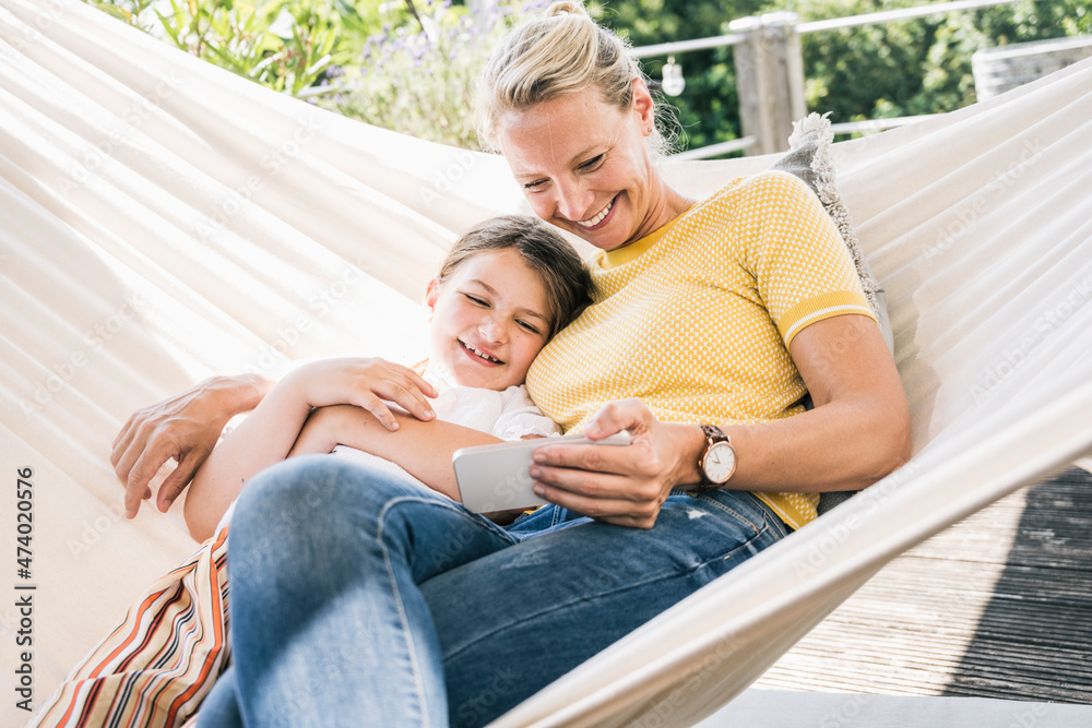 Mother and daughter smiling while relaxing on hammock at balcony Mother and daughter smiling while relaxing on hammock at balcony