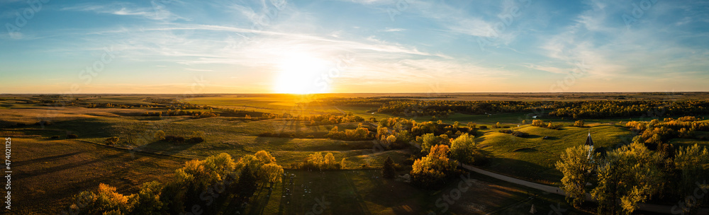 Aerial panorama of a sunset over the gentle rolling hills of the Great Plains with trees in their autumn colors in North Dakota.