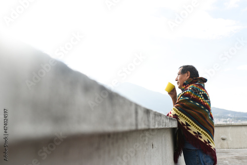 Indigenous man drinking coffee while leaning on retaining wall at rooftop photo