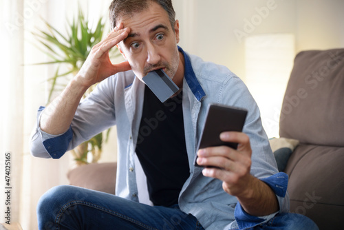 Surprised man with online purchase biting credit card at home