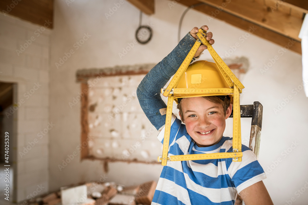 Smiling boy holding pocket rule of house shape at attic during renovation Smiling boy holding pocket rule of house shape at attic during renovation