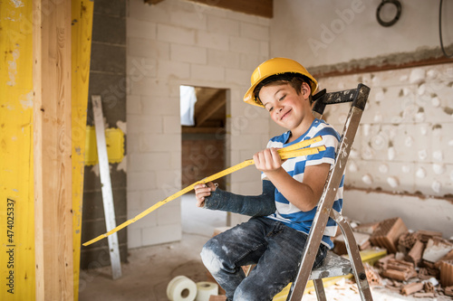 Smiling boy looking at pocker rule while sitting on ladder at construction site photo