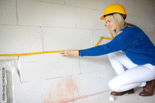 Female building contractor measuring wall with folding ruler while crouching at site