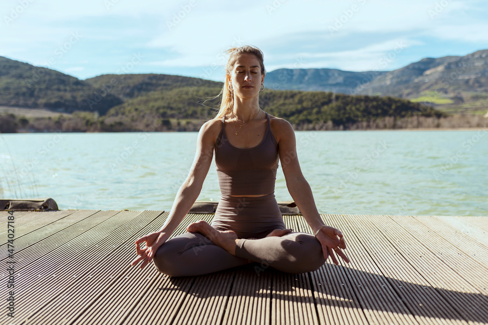 Woman with eyes closed meditating while sitting in lotus position on sunny day