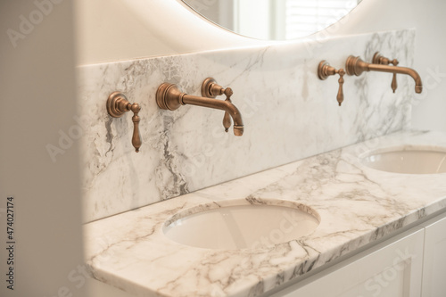 Bathroom with marble sinks with bronze taps and illuminated mirror photo