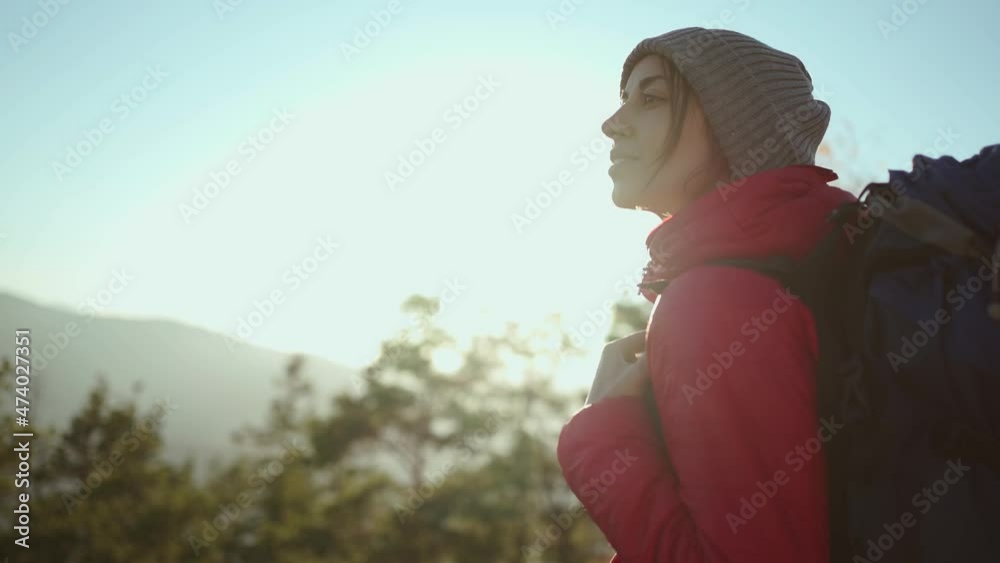 slow motion portrait young woman in red jacket on mountain top at sunset with sun raises and flares. girl enjoying nature and looking confident and happy with her hiking expedition outdoors. slow motion portrait young woman in red jacket on mountain top at sunset with sun raises and flares. girl enjoying nature and looking confident and happy with her hiking expedition outdoors.
