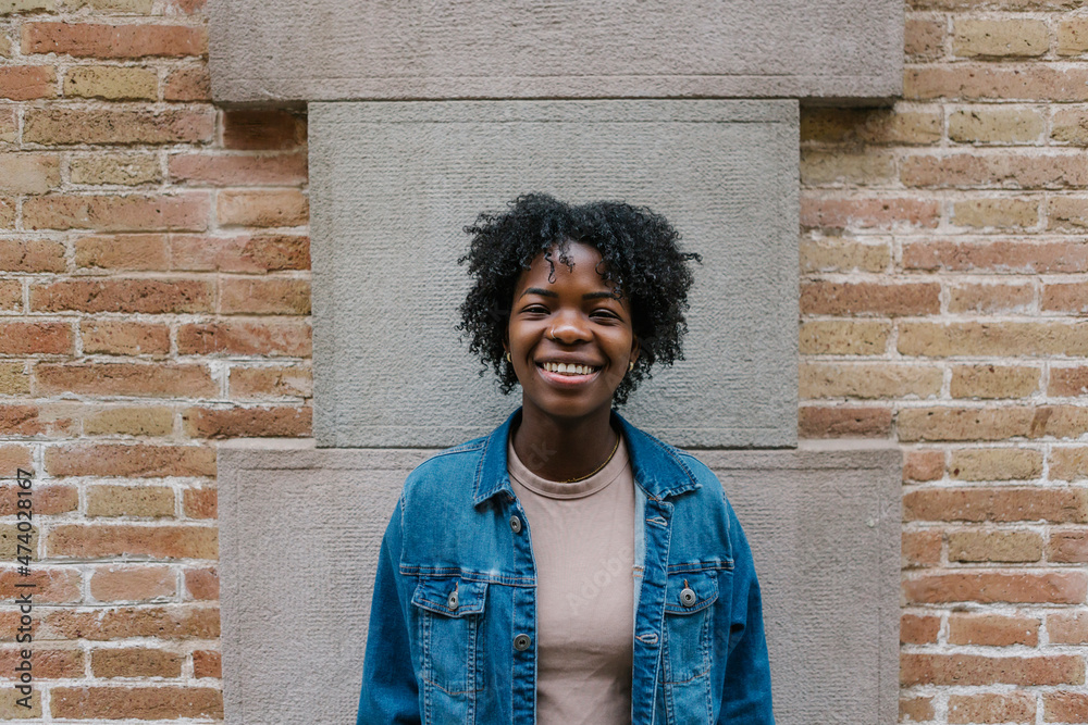 Cheerful woman wearing denim jacket standing in front of wall Cheerful woman wearing denim jacket standing in front of wall