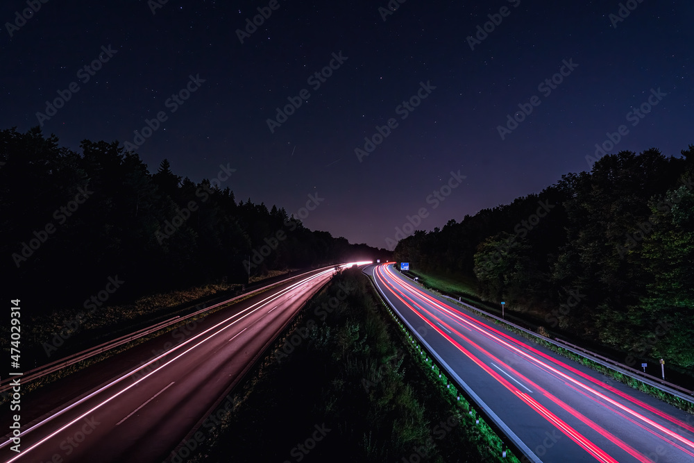 A german Autobahn at night with lighttrails of the fast driving cars in red, wallpaper photo for a high speed concept.